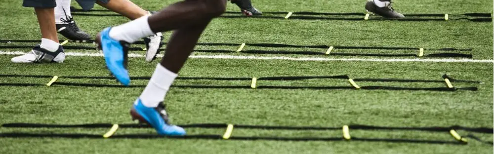 A narrow view of men using an agility ladder on a grass field