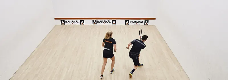 Two squash players on a squash court performing a drill