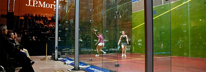 Two professional squash players playing on a glass court