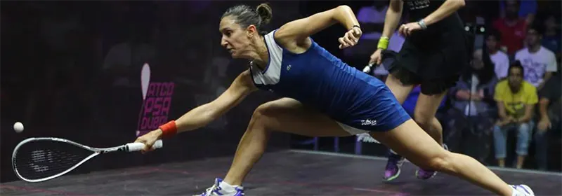 A professional squash player reaching for a ball