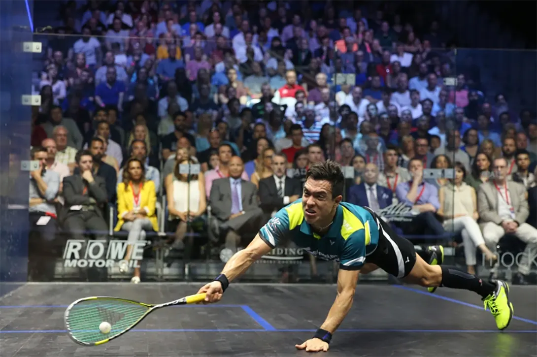 A professional squash players dives to reach tghe ball