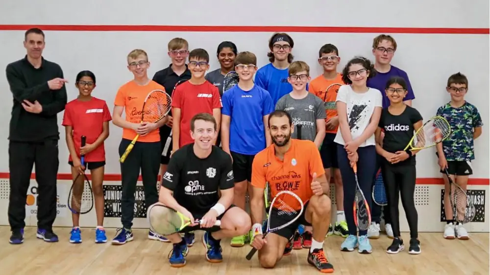 A group of juniors squash players behind two crouching pros