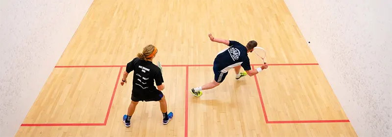 Two men playing squash with goggles