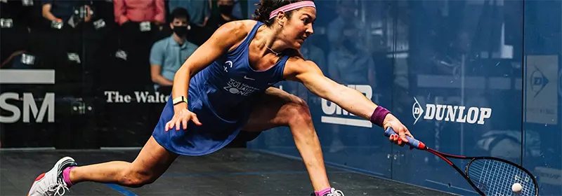 A professional squash player reaches for the ball