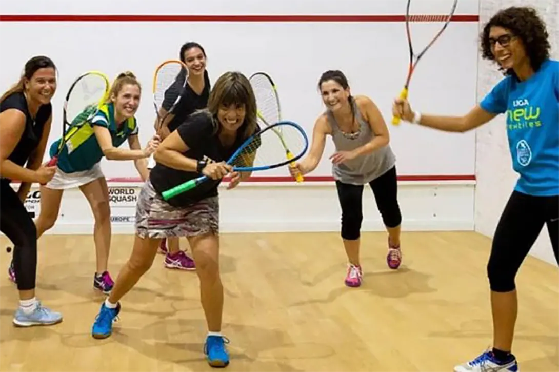 A few ladies showing their squash rackets and smiling