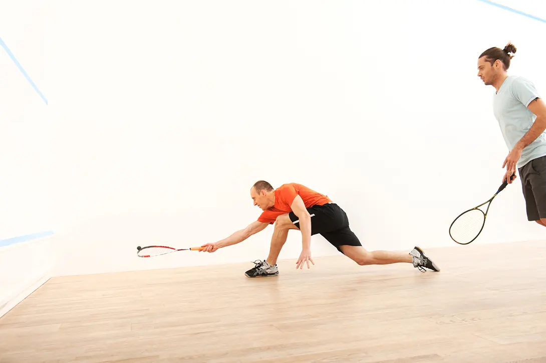 A male squash player lunges to reach a shot and plays a lob