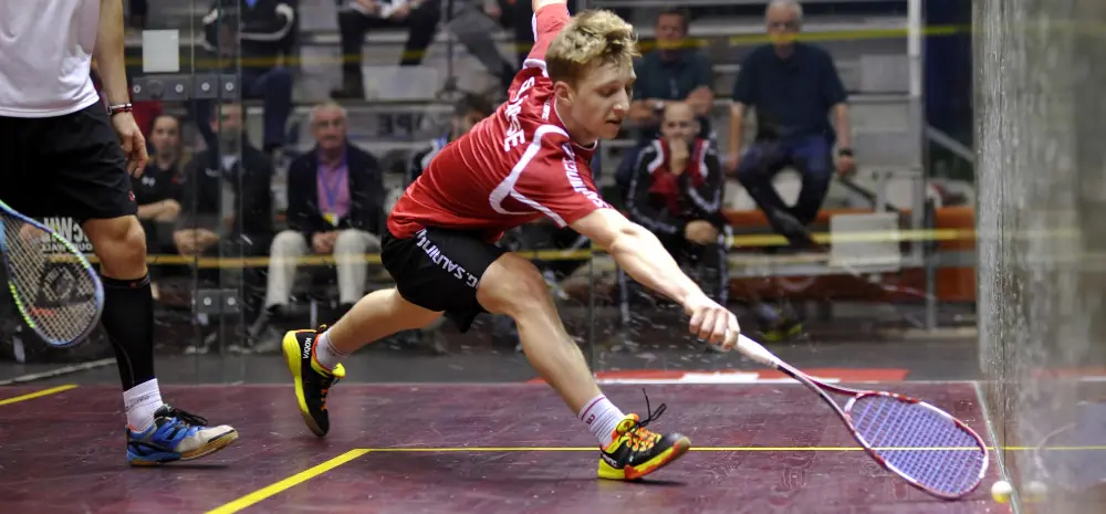 A professional squash plaeyr reaching for a difficult shot