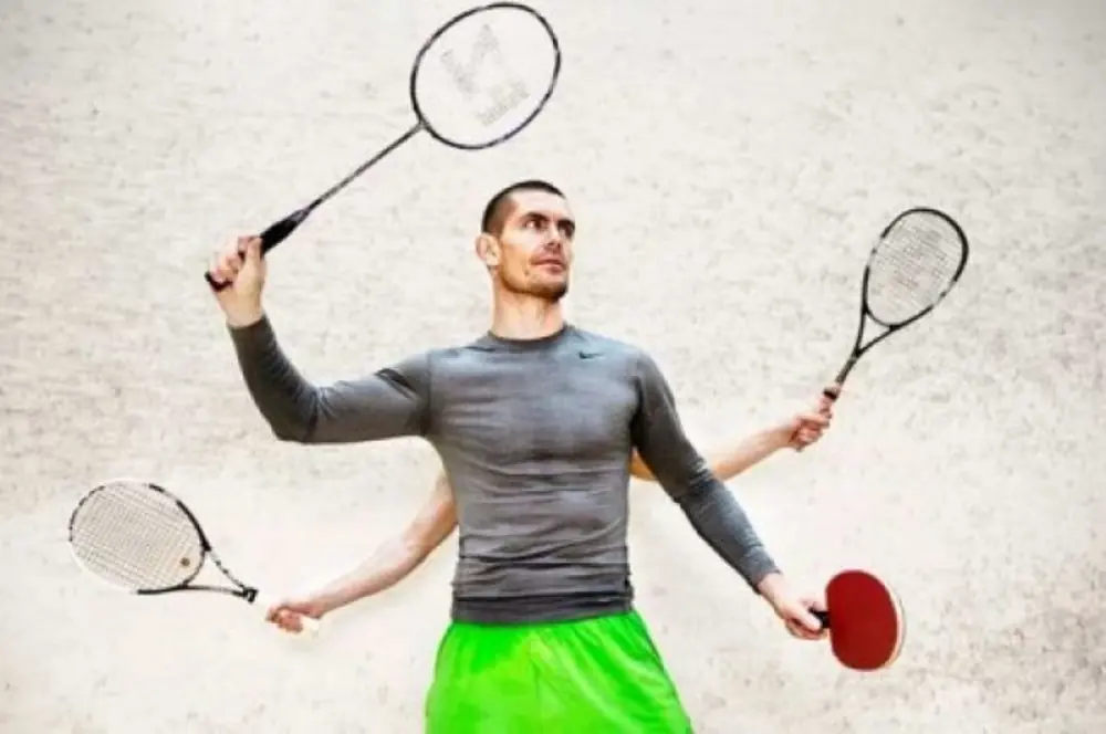 A man standing holding two rackets with somebody behind him holding two others