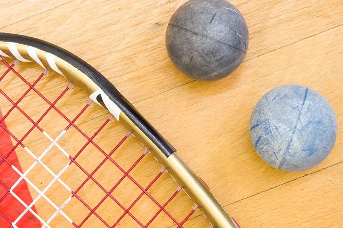 A squash racket and two shiny squash balls, lying on the wooden squash floor