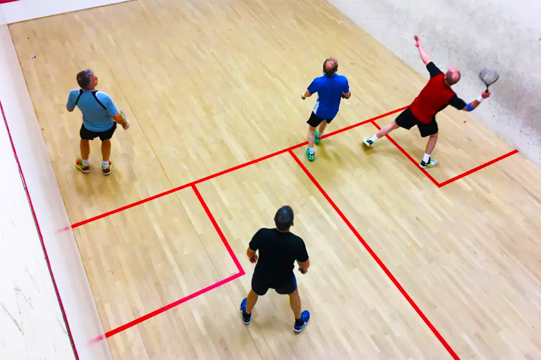 The view from the balcony of a singles squash court with a doubles match being played.