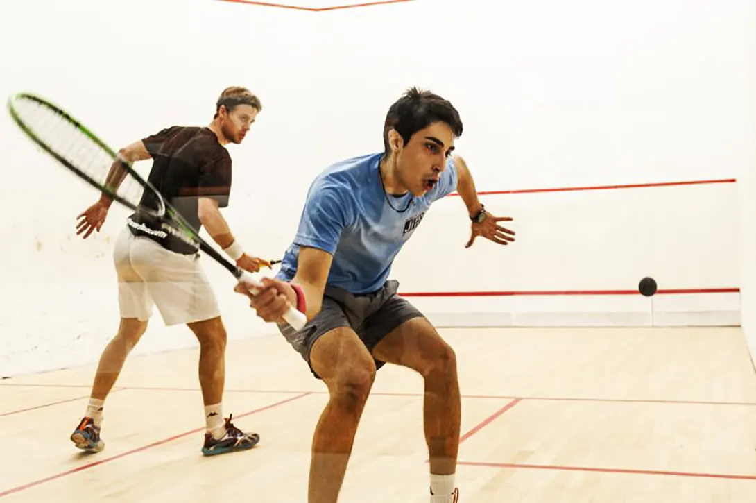 Two high-level squash players in the middle of a rally.