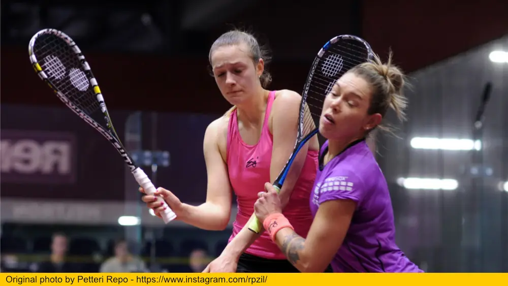 Two women playing squash bumping into each other